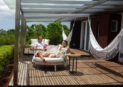 A couple sitting on a natural wooden sofa outside, on the deck of Tortuga Villa